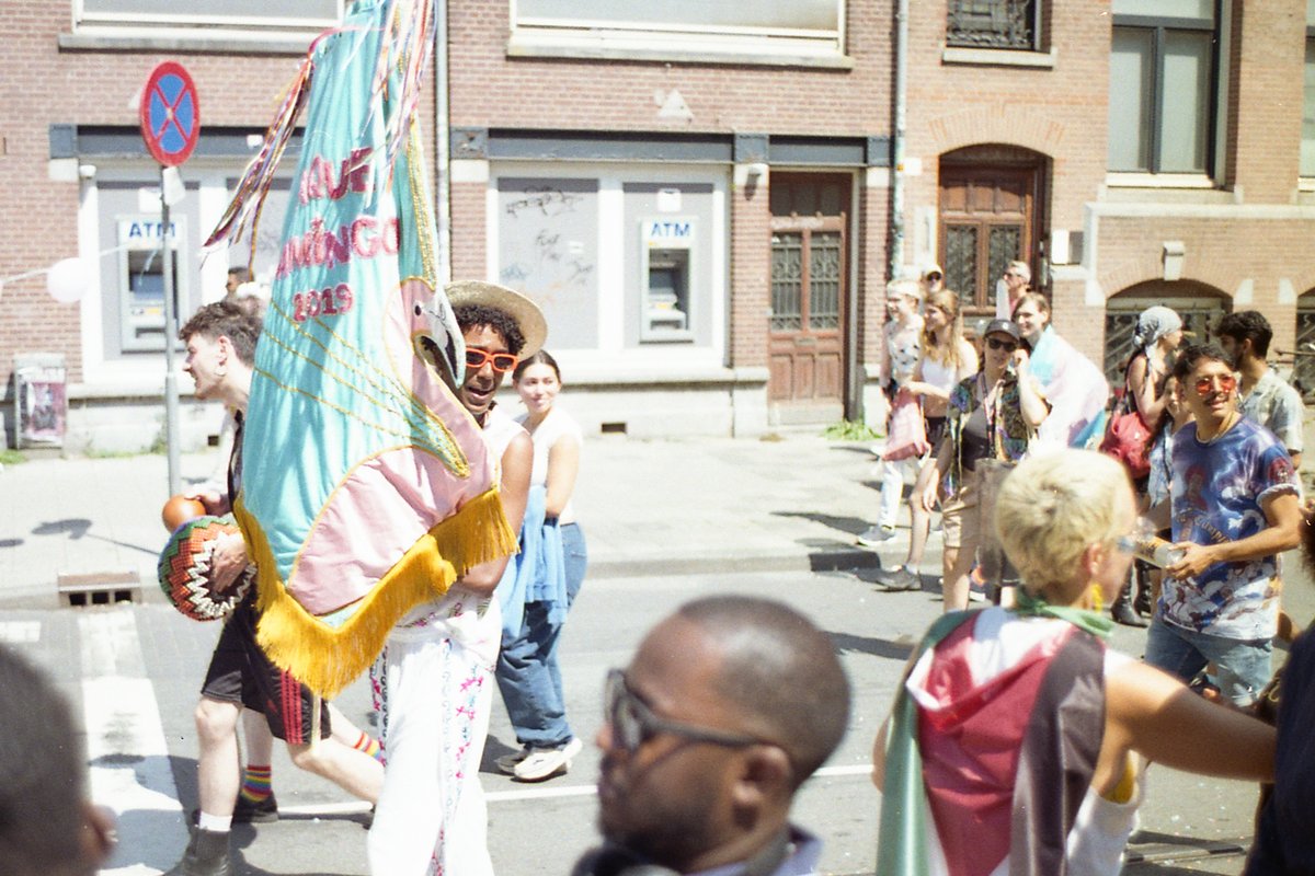 This image captures a lively street festival. Among the crowd, a person is holding a large kite, possibly participating in a parade or festive event. 