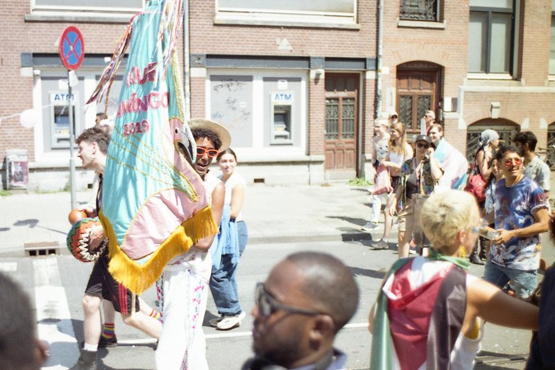 This image captures a lively street festival. Among the crowd, a person is holding a large kite, possibly participating in a parade or festive event.