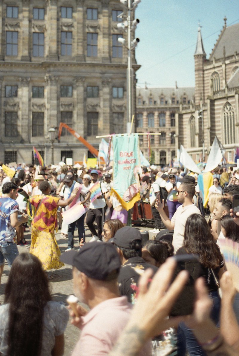 The image captures a vibrant scene of a large gathering on a city street. Various people are seen engaging in activities such as dancing and socializi