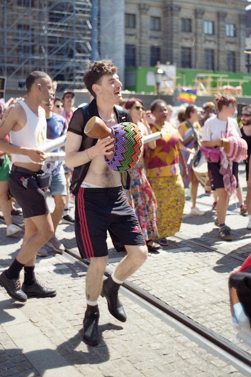 The photo captures a lively scene at a carnival. In the center of the frame, a man with sunglasses and a blue hat is holding a beige stuffed animal, s