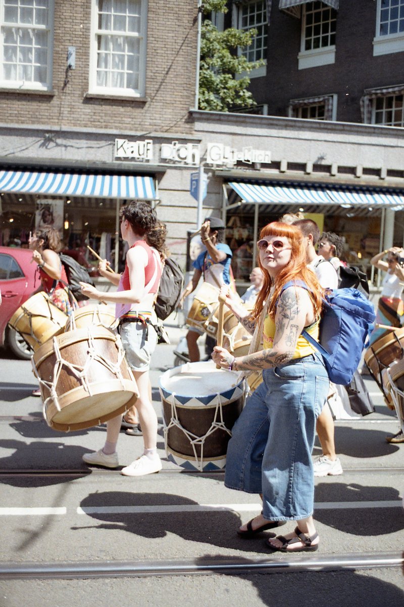 This photo captures a lively street scene. A group of people are playing musical instruments on the sidewalk. Some are holding percussions like drums