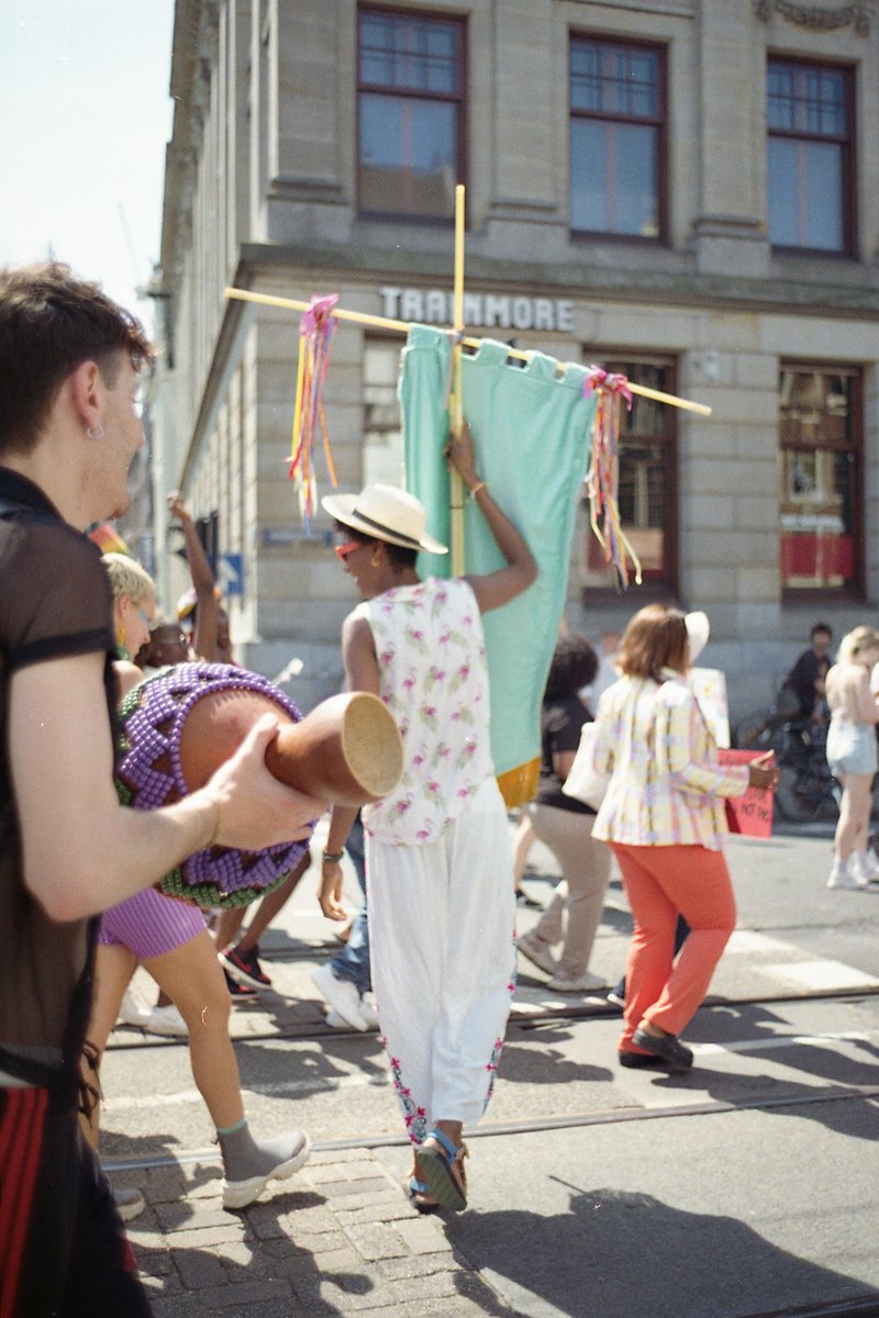 This image depicts a lively scene from a parade. The main focus is on two individuals who are dancing with masks and colorful outfits. One individual