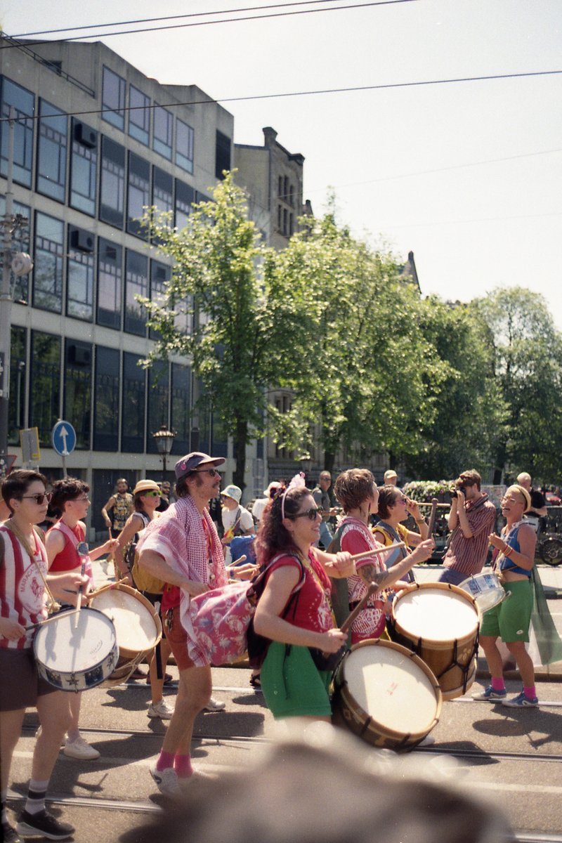 A lively scene of a parade unfolds. The main focus is a group of people passionately playing large drums, their rhythmic beats echoing through the str