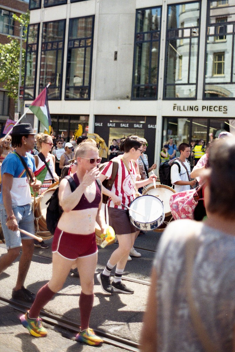 This image captures a vibrant scene from a parade. A group of people, dressed as runners with marathon numbers, are marching down the street. They car