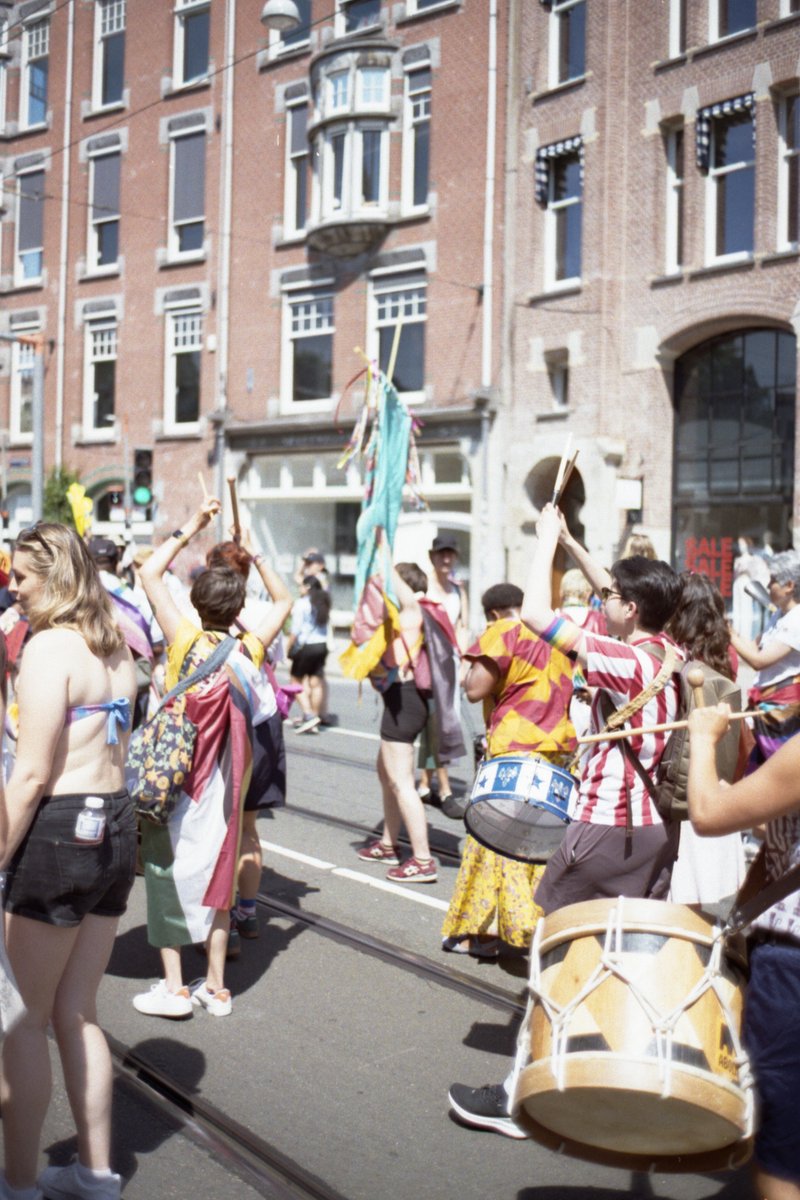 The photo depicts a lively street festival. A large crowd of people are seen holding up their hands to the sky, possibly as a gesture of appreciation