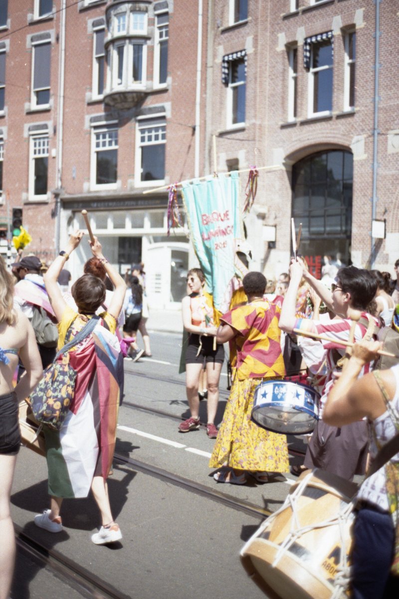 A group of people in the street, some holding instruments and flags. They are playing instruments and marching together. The scene takes place in fron