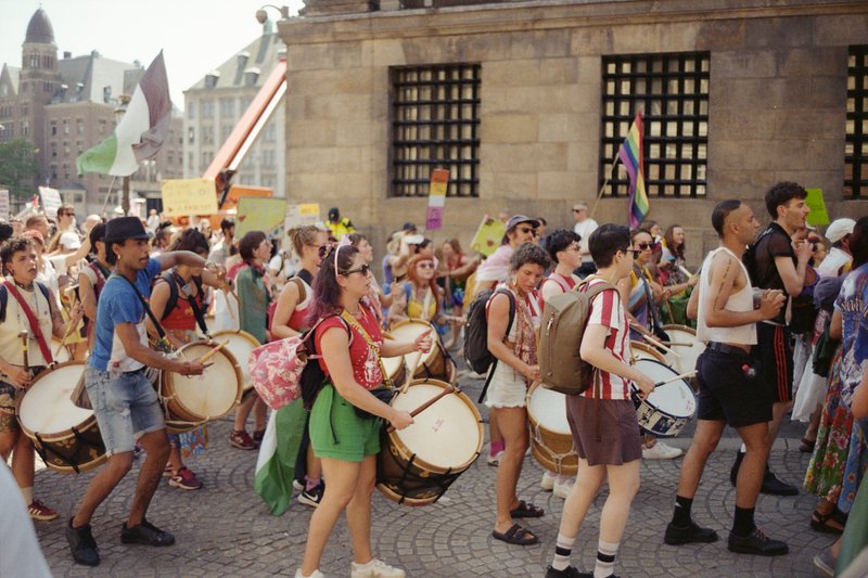 This is a color photograph capturing a public outdoor event. A crowd of people is seen marching down a street, some holding signs and banners with slo