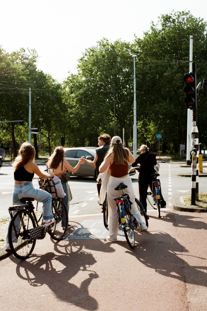 This image shows a group of people in the foreground riding bicycles on a sidewalk. They are traveling down the street towards a traffic light and oth