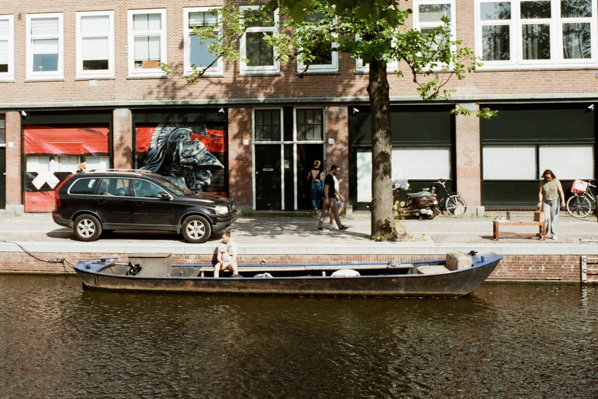 This image depicts a peaceful scene of a narrow canal with a small boat on the water. Alongside the canal, there is a row of businesses including a re