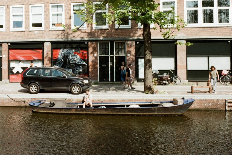 This image depicts a peaceful scene of a narrow canal with a small boat on the water. Alongside the canal, there is a row of businesses including a re