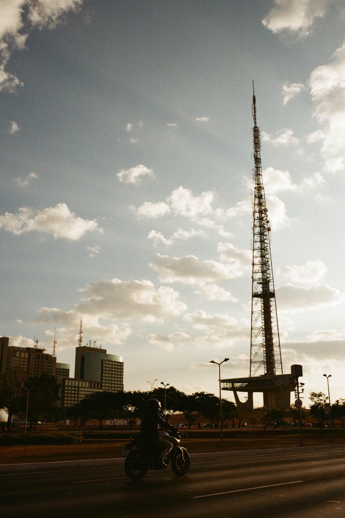 The image depicts a scene from a city street at dusk. In the foreground, there's a tall antenna tower standing out against the skyline. The sky is ado