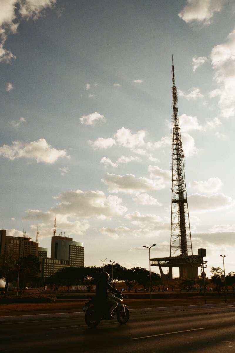 The image depicts a scene from a city street at dusk. In the foreground, there's a tall antenna tower standing out against the skyline. The sky is ado