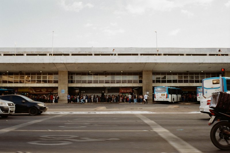 An overhead image of an airport terminal with a large white building featuring a long flat roof. The foreground shows traffic lights and a street corn