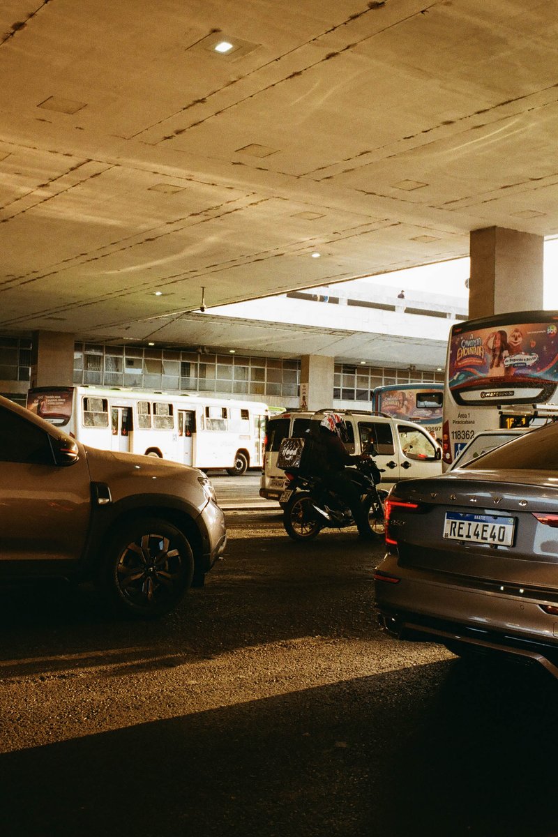 The image shows a multi-lane highway during the evening. There is heavy traffic with numerous vehicles, including cars and buses. Traffic lights are v