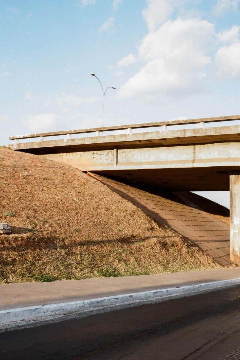 A color photograph of a single-lane concrete overpass during daytime. The overpass is brown and stretches across the image. It's set against a backdro