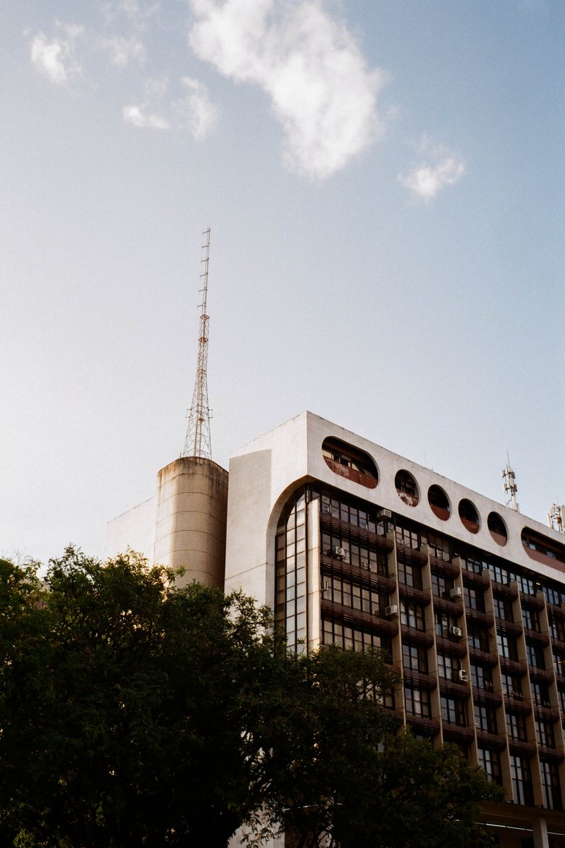 The image depicts a large, modern building with a distinctive design. The architecture features multiple levels and flat roofs. Notably, the facade is
