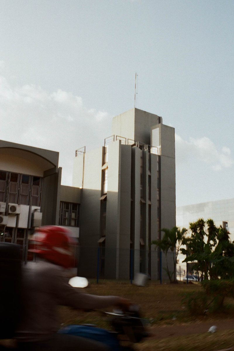 This is a cityscape photograph featuring a tall building with several levels. In the foreground, there's a blurred figure riding a motorcycle. The sce