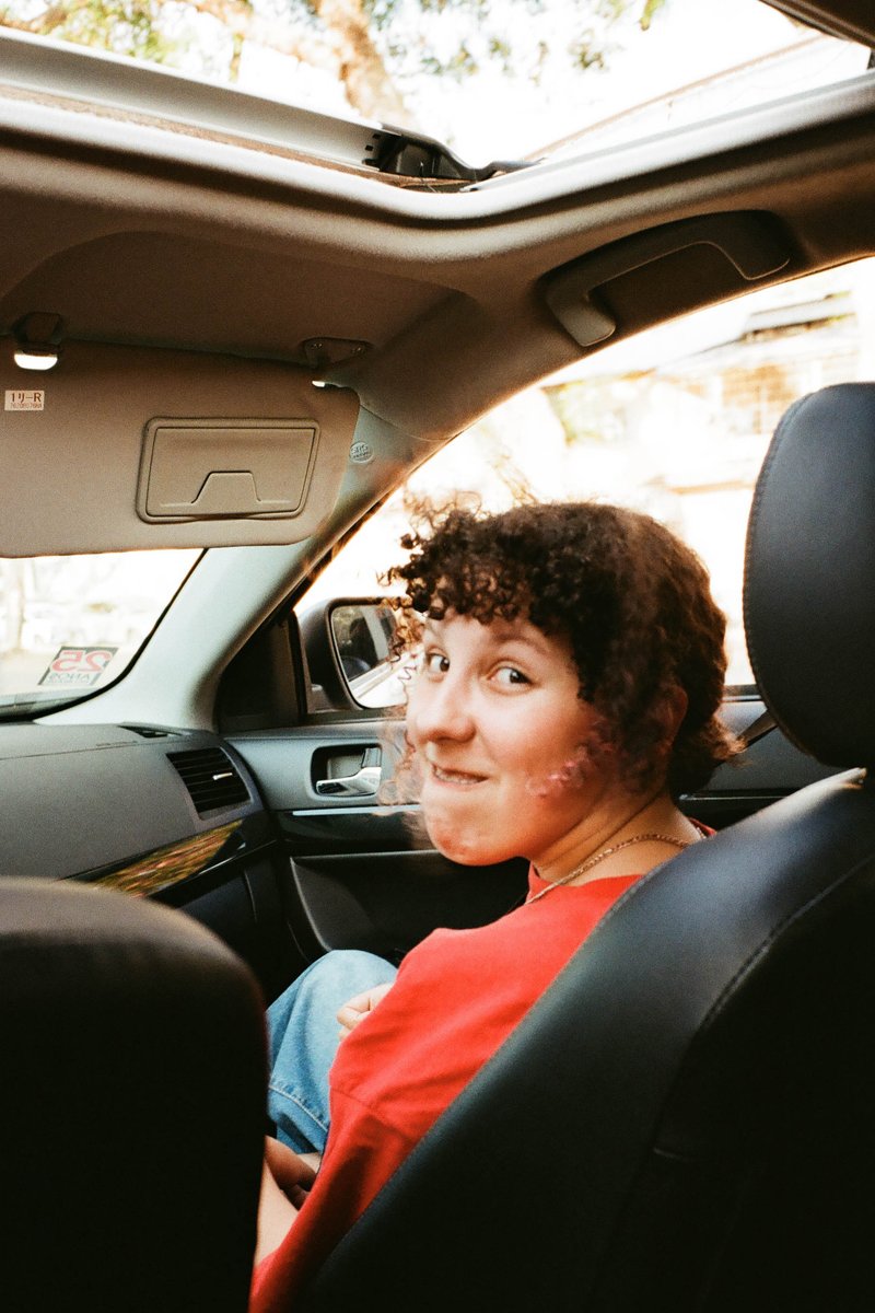 This is a photo of a person inside a car. The individual is seated and appears to be relaxed, possibly enjoying the ride or waiting for someone. They