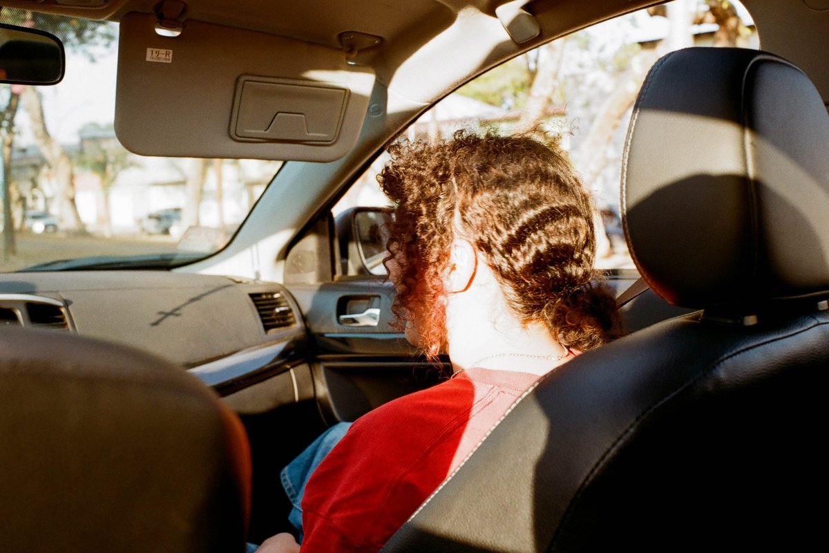 The photo shows the inside of a car from the perspective of someone sitting in the back seat. The person is wearing glasses and appears to be looking 