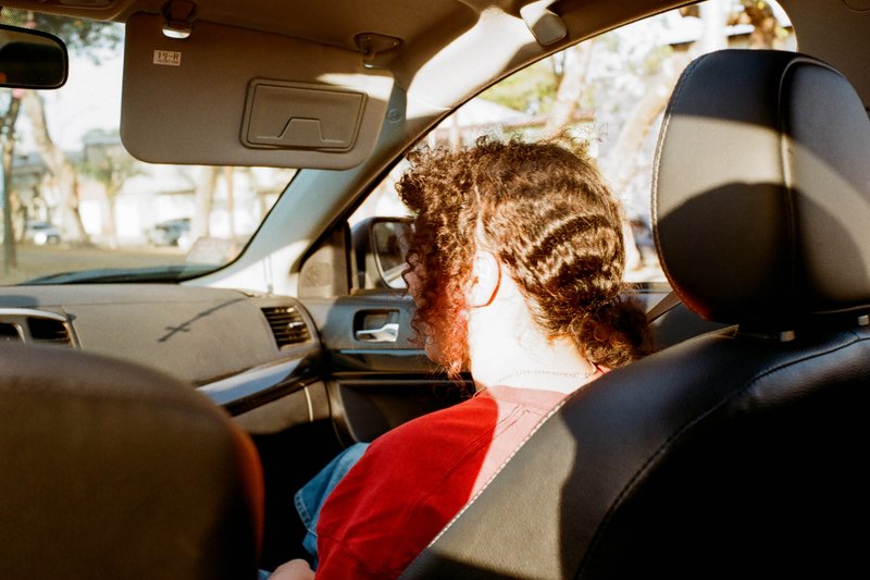 The photo shows the inside of a car from the perspective of someone sitting in the back seat. The person is wearing glasses and appears to be looking