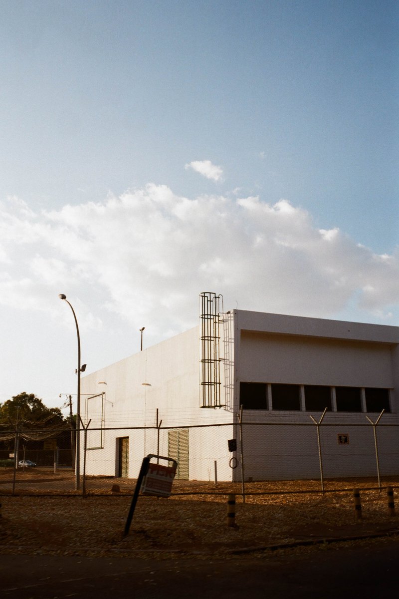 The image features a large white building with multiple windows and what appears to be a red and white sign. It's situated in front of a sky backgroun