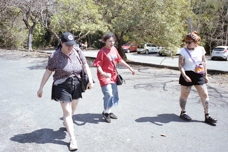 A group of people walking together on a street. Some are carrying handbags and backpacks. They appear to be engaged in conversation as they move along