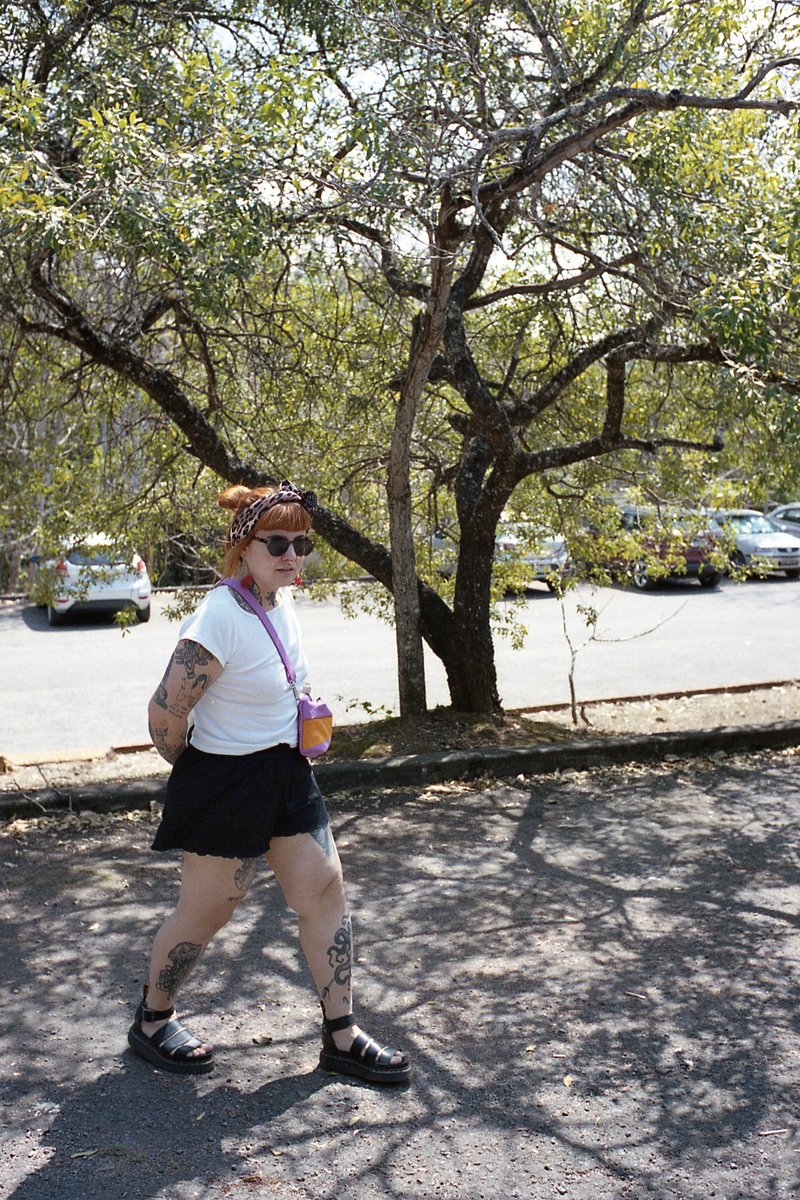 The image captures a woman walking on the sidewalk. She's holding a cup and is wearing shorts and a t-shirt. Her hair is styled in bangs and she has t