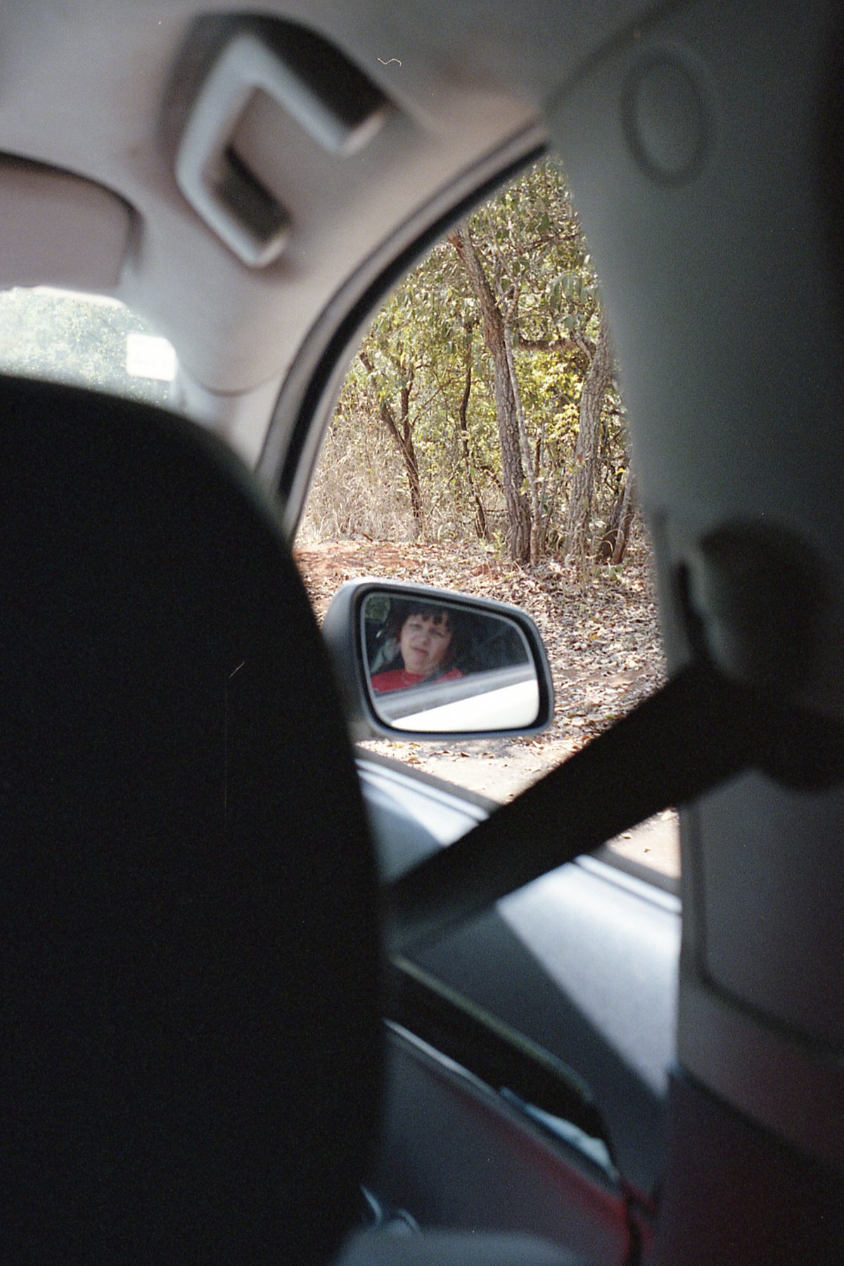 This is a black and white photo showing the interior of a car. Through the window on the left side of the vehicle, you can see a person sitting in the