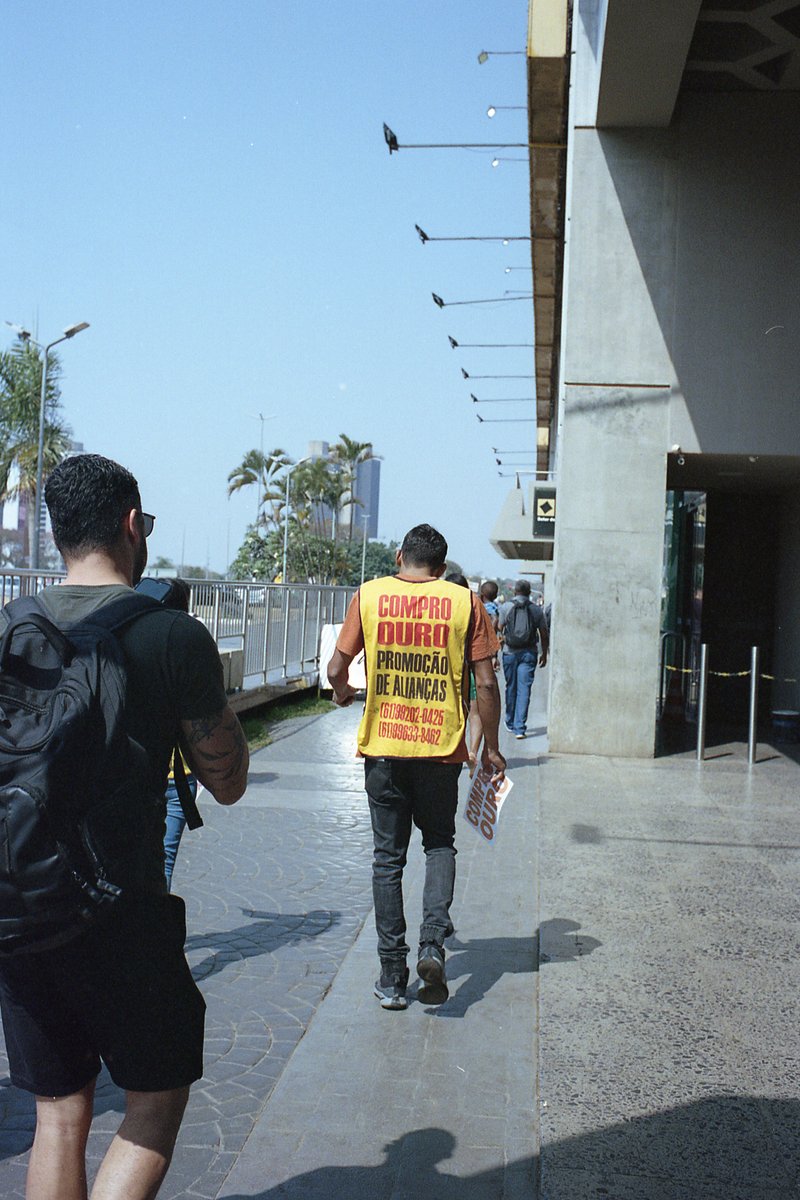 The photo depicts an outdoor scene, likely taken from inside a vehicle. A man is walking past, dressed in casual clothing and wearing a yellow safety