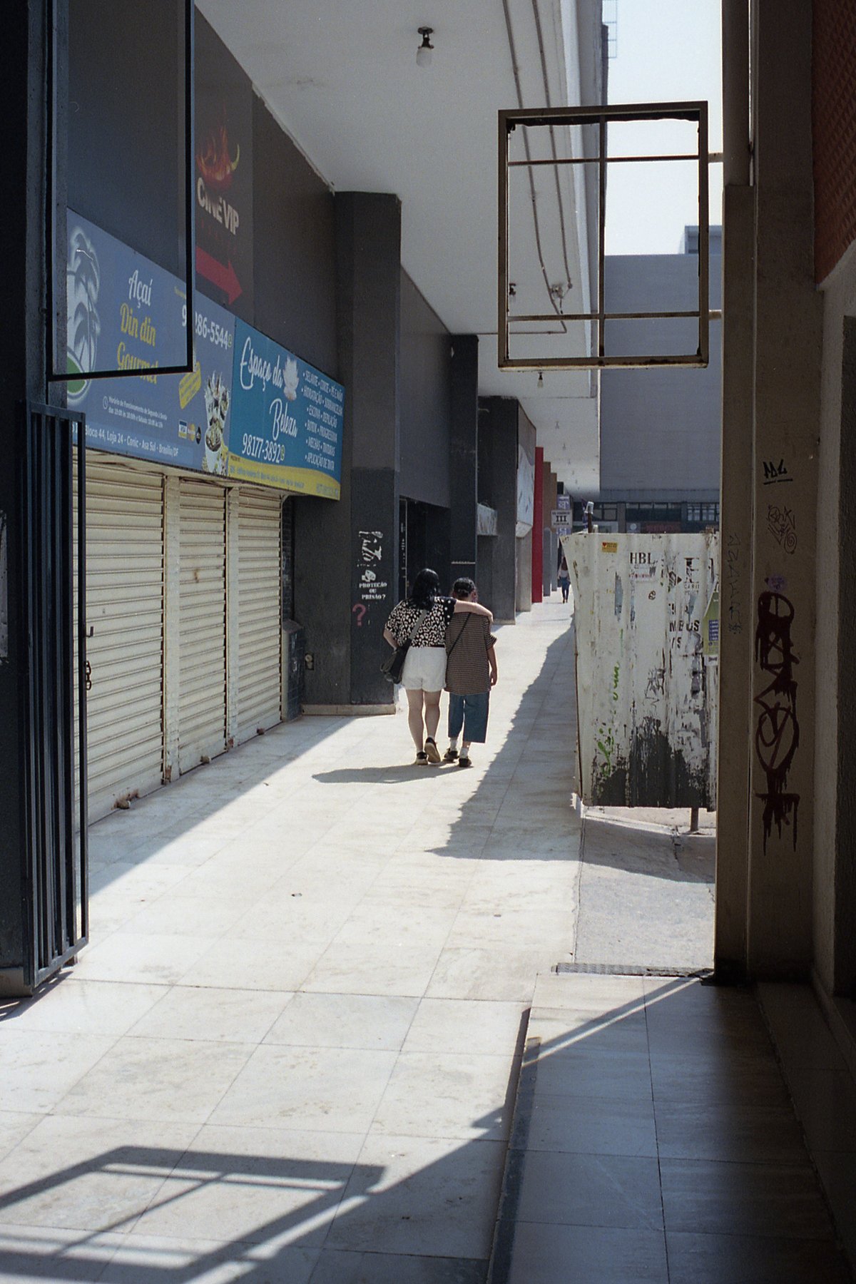 A person walking down a narrow sidewalk between buildings. The area appears deserted with no people visible besides the one walking. Buildings on eith