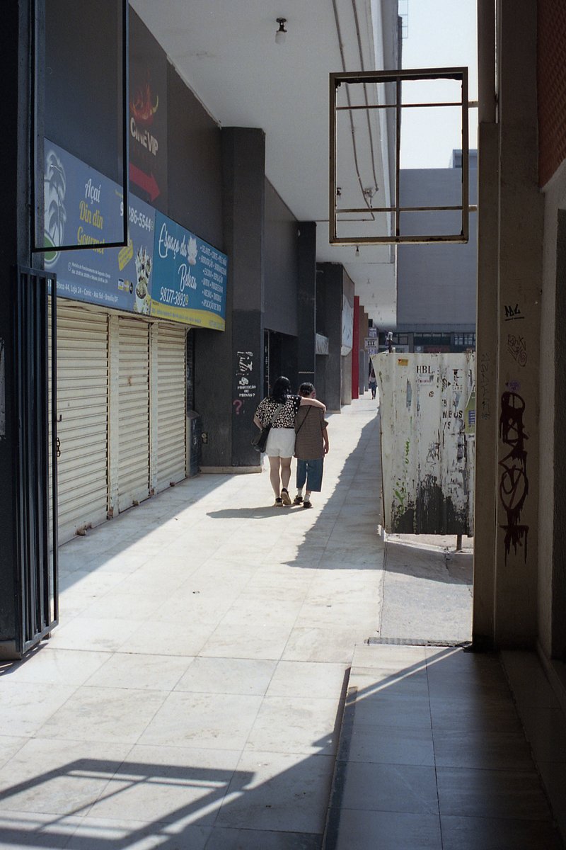 A person walking down a narrow sidewalk between buildings. The area appears deserted with no people visible besides the one walking. Buildings on eith