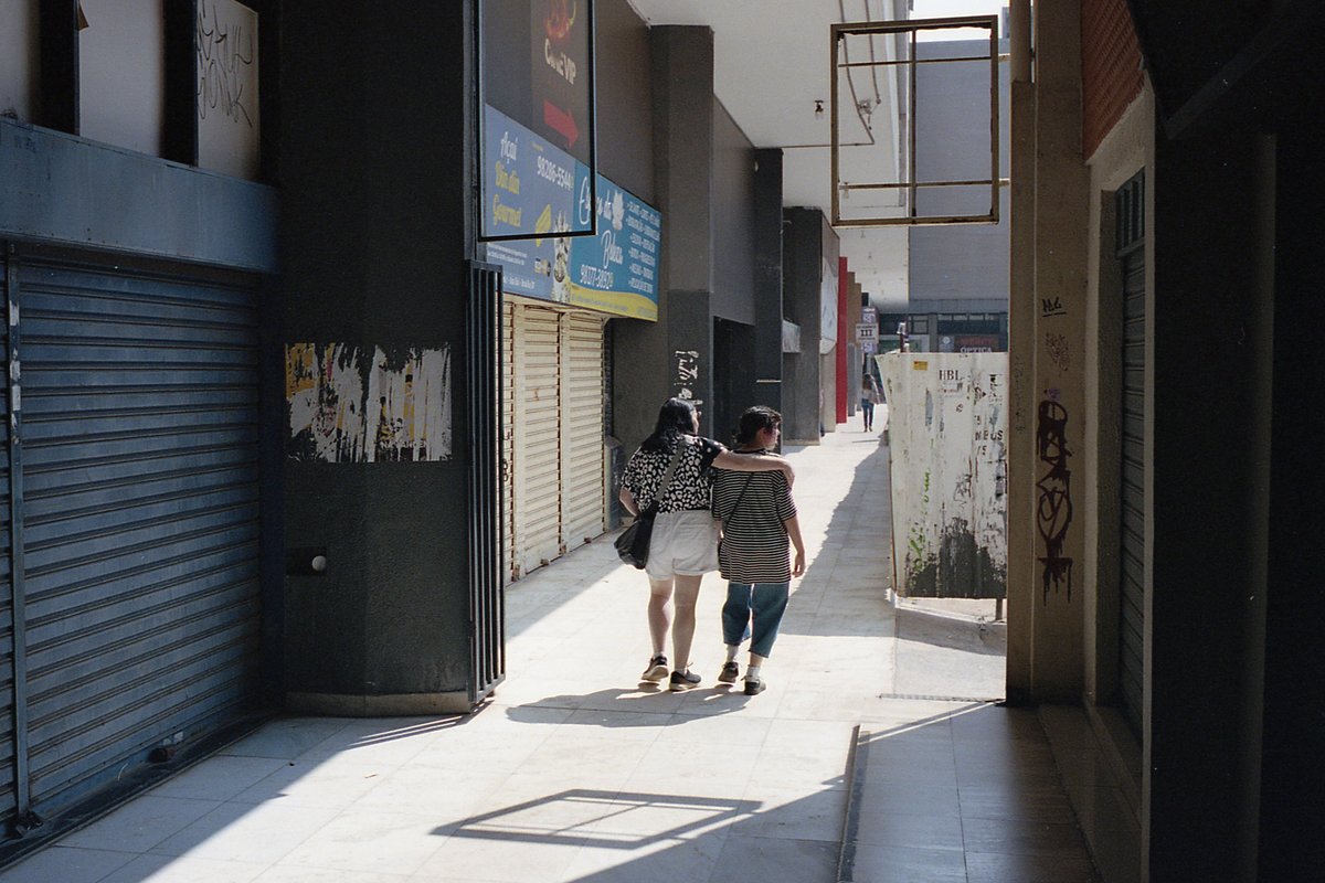 The image captures a tranquil street scene. A couple is walking away from the camera, perhaps enjoying a romantic stroll. They are passing by various 