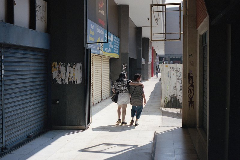 The image captures a tranquil street scene. A couple is walking away from the camera, perhaps enjoying a romantic stroll. They are passing by various
