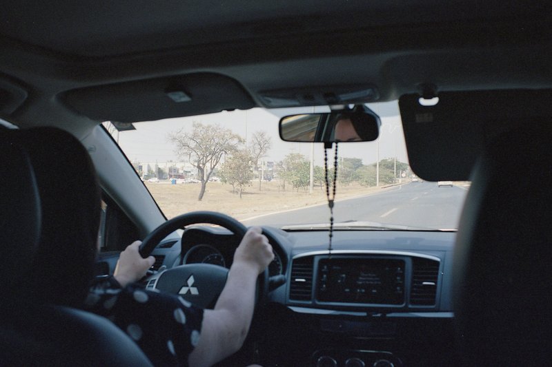 The image is a real photo depicting the interior of a car from the perspective of the back seat. A person's hands are visible on the steering wheel, w