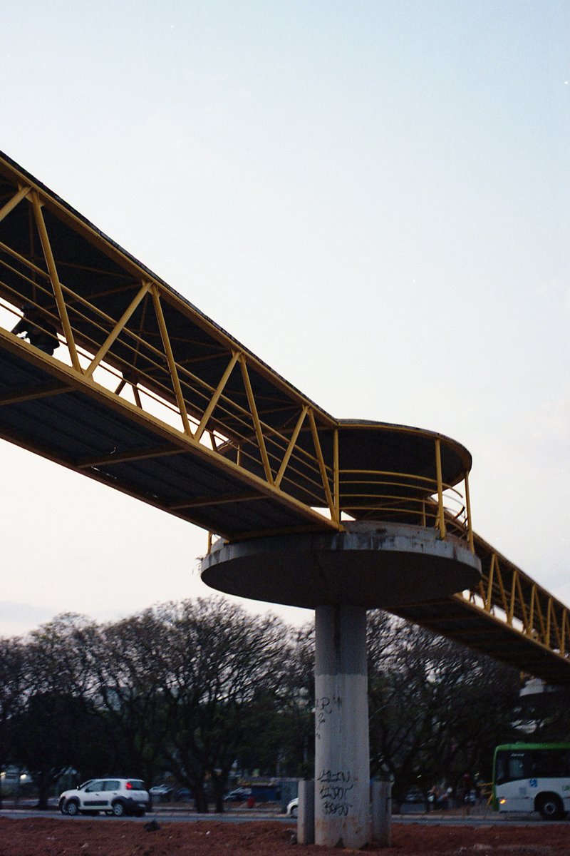 This image depicts a highway overpass with yellow railings. The structure is supported by sturdy concrete pillars and appears to be undergoing constru