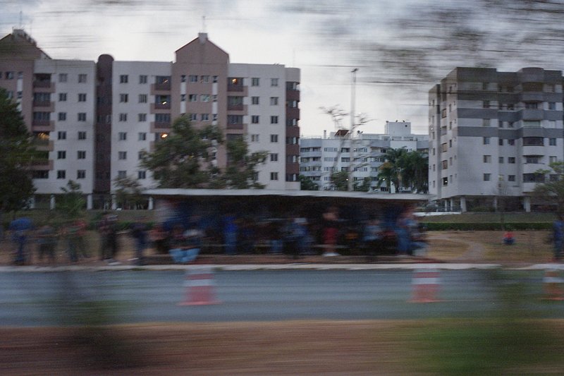 The image captures a vibrant scene of an urban setting at dusk. A bus is driving past tall buildings, creating a dynamic sense of motion against the s