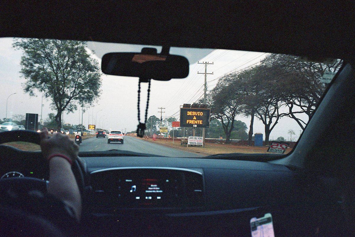 A person sitting in a car at night, driving on a city street with a traffic sign visible. The car is equipped with a handicap tag.