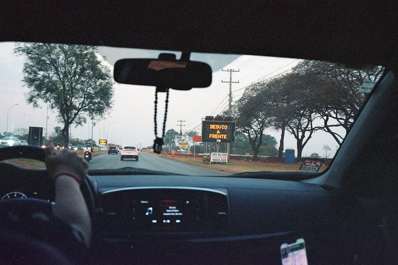 A person sitting in a car at night, driving on a city street with a traffic sign visible. The car is equipped with a handicap tag.