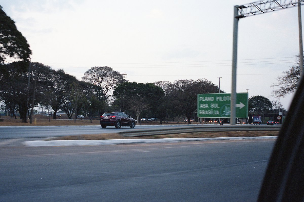 The image is a nighttime shot of a highway overpass with various signs indicating directions and distances. A car drives on the highway below. The sky