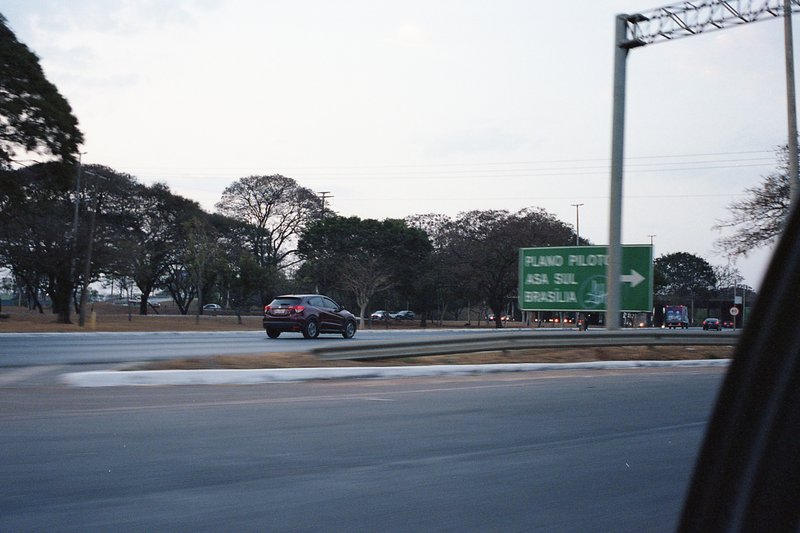 The image is a nighttime shot of a highway overpass with various signs indicating directions and distances. A car drives on the highway below. The sky