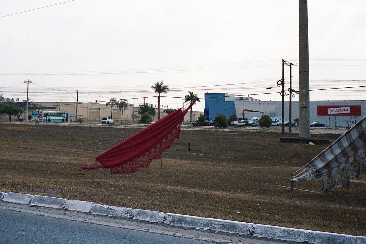 The image shows a street scene during the day. The focus of the image is on two objects: a red flagpole and a piece of bright red clothing that appear