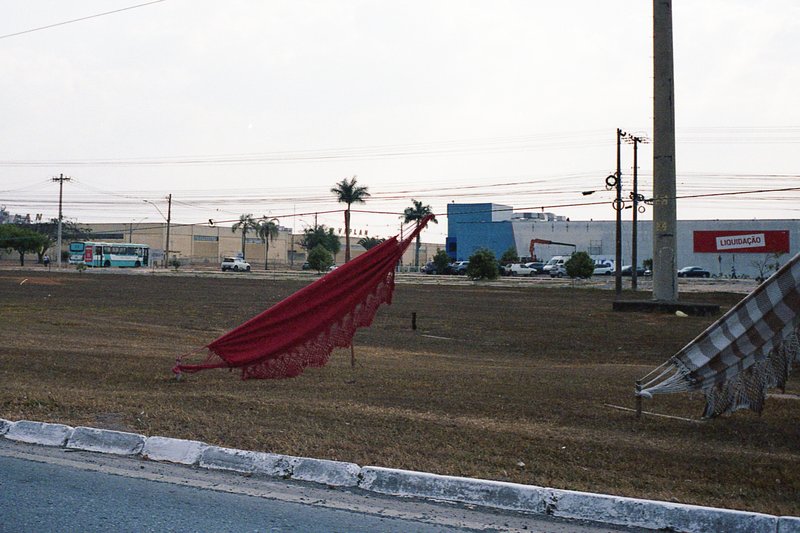 The image shows a street scene during the day. The focus of the image is on two objects: a red flagpole and a piece of bright red clothing that appear