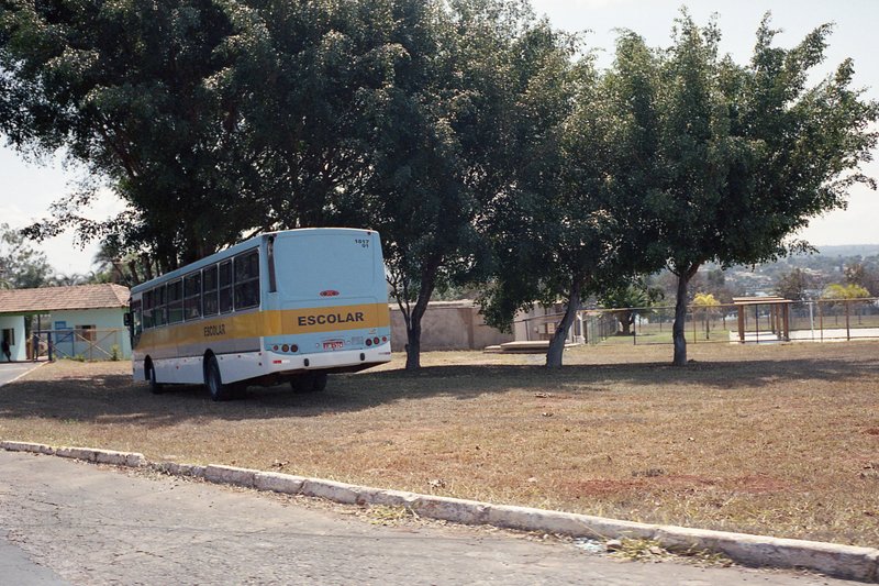 This is a color photo featuring an outdoor scene. In the foreground, there's a light blue school bus parked on the side of a paved road. The bus is ma