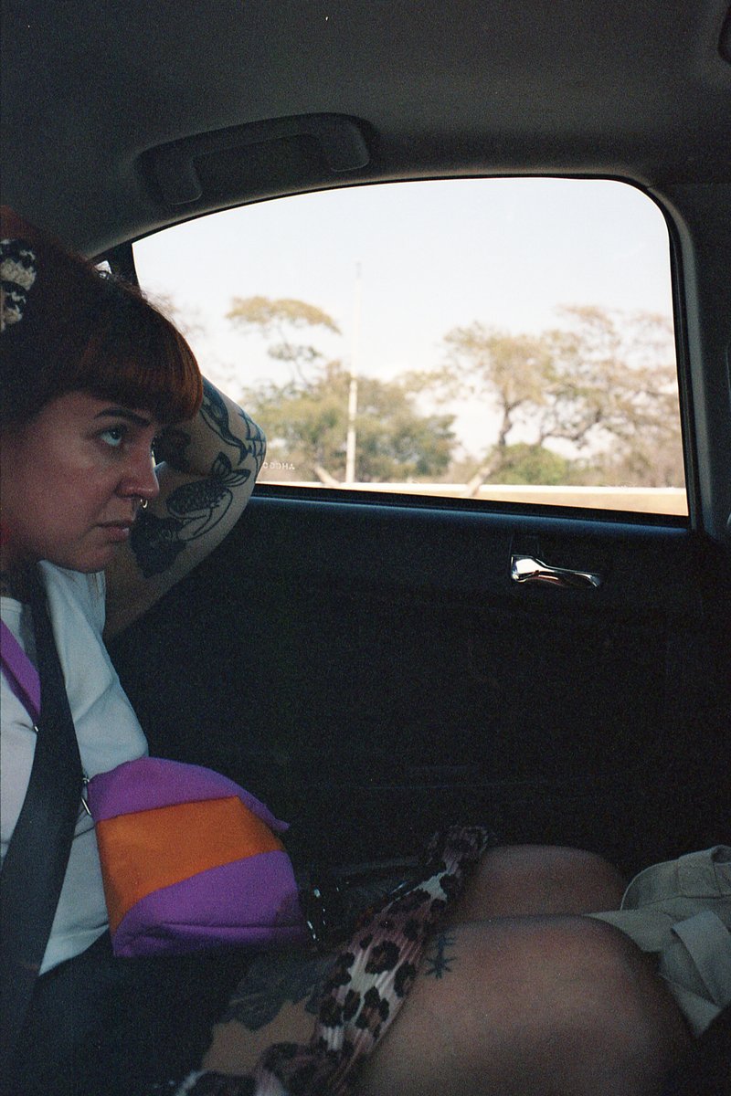 The image is a candid photograph featuring a person seated inside a vehicle. The individual appears to be looking out of the window with their head re