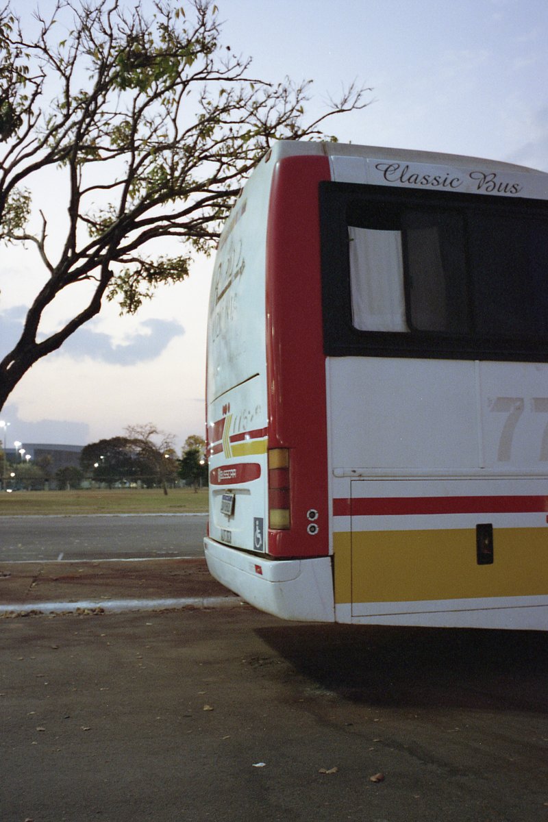 This image features a large red bus parked at night. The bus is facing towards the left side of the photo and is prominently displayed. It has a yello