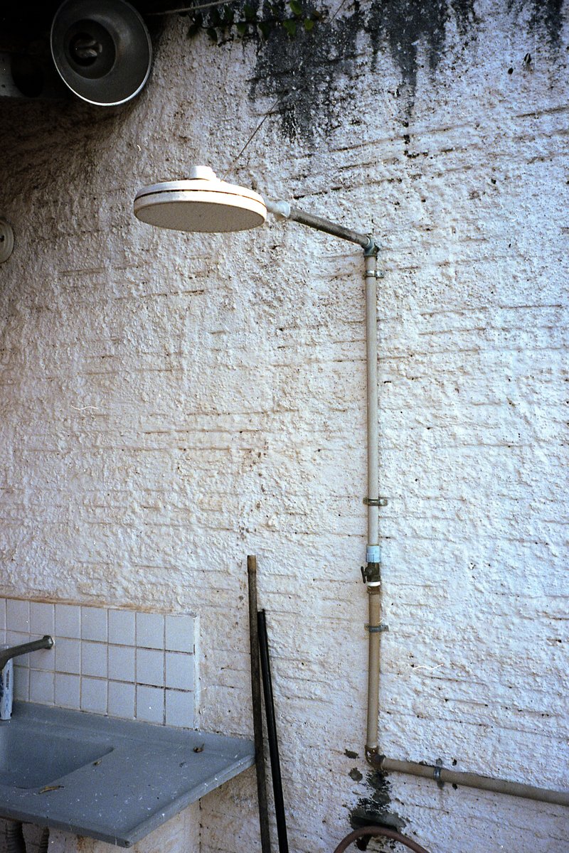 The image showcases an old-fashioned kitchen. Dominating the scene is a white sink, situated below a window. A black and silver shower head, reminisce