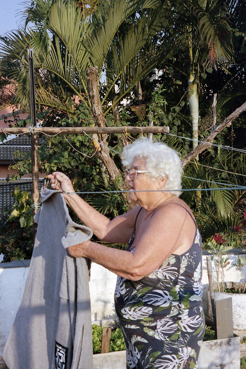 A woman is outside near a clothesline. She stands next to the line with her back turned to the camera. The woman appears to be hanging clothes on the