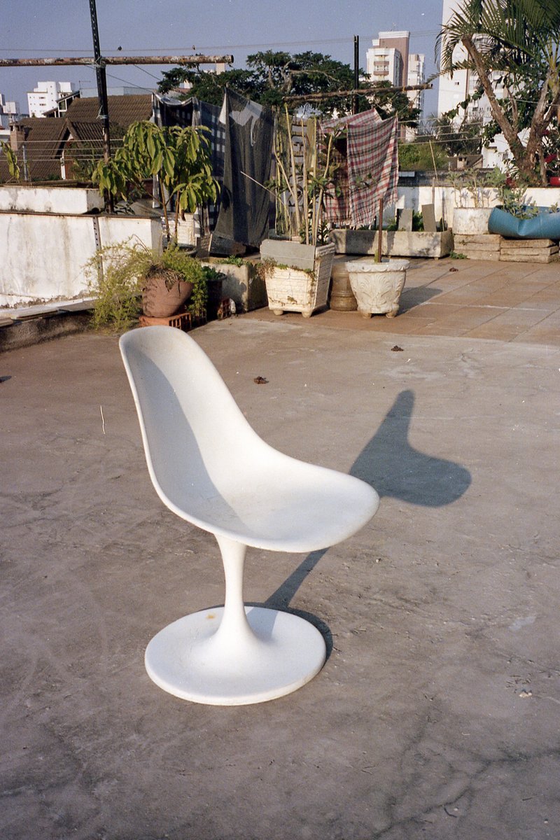 In the image, a white chair with a high back and minimalist design is placed on a concrete floor. The chair's unique shape stands out against the indu