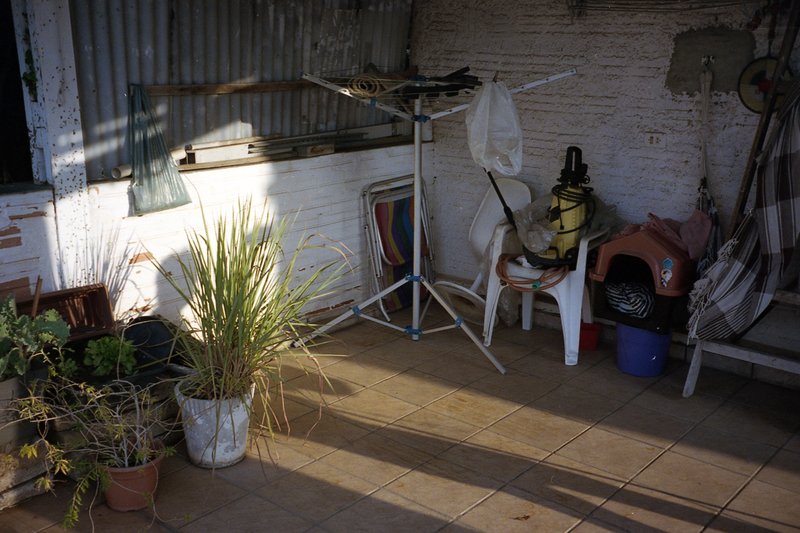 The image is a photograph of an outdoor space that appears to be the lower level or patio area of a house. It is daytime and sunlight illuminates the
