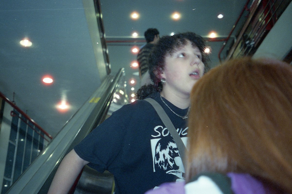 A photograph capturing a person on a train platform. The individual is looking upwards and appears surprised or curious. They are standing near a meta